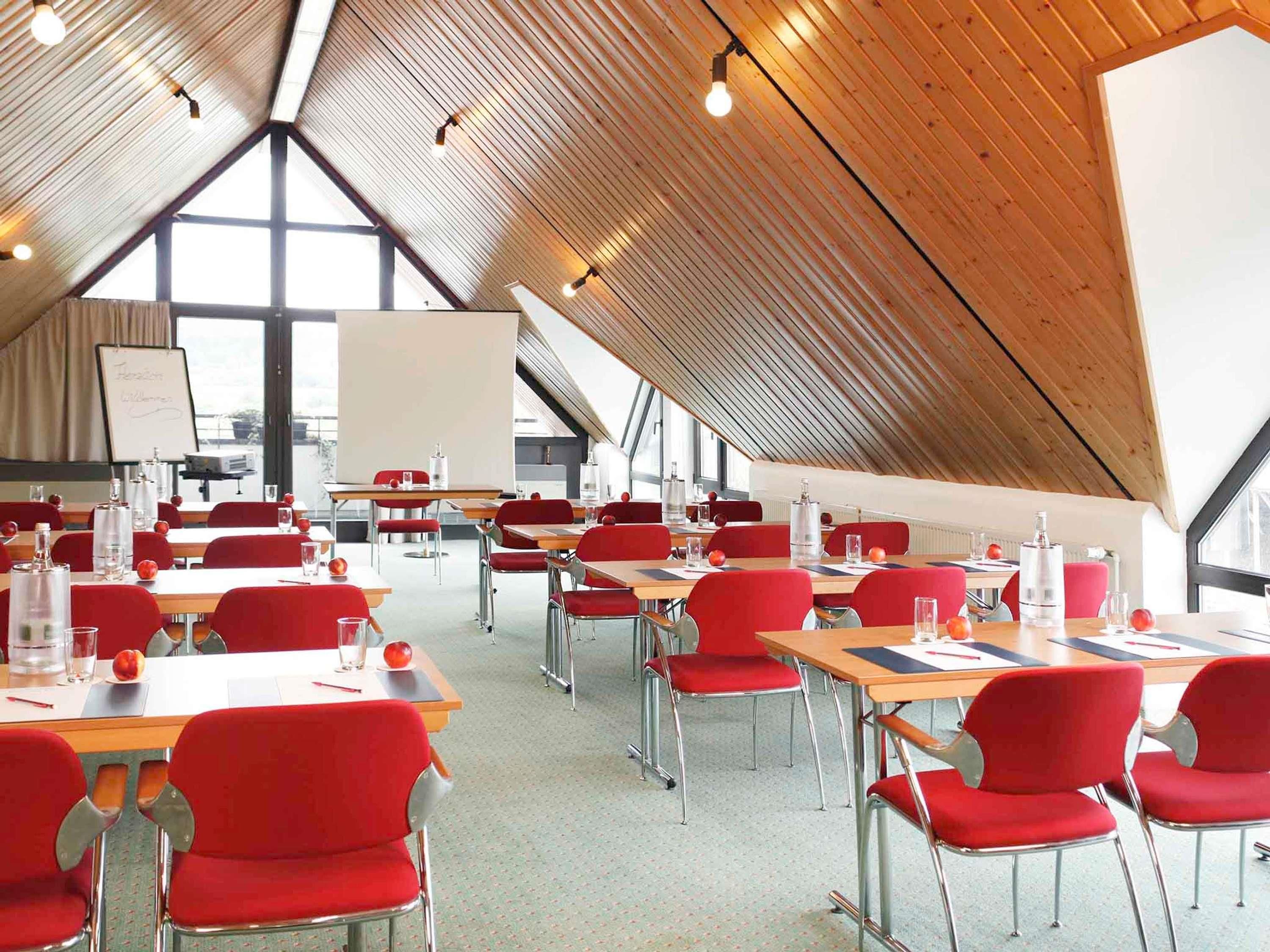 Een vergaderruimte met rode stoelen en tafels, een whiteboard en grote ramen.