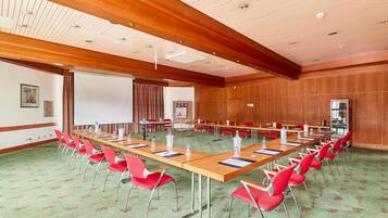 A conference room with a long table, red chairs, a projector screen, and wooden panel walls.