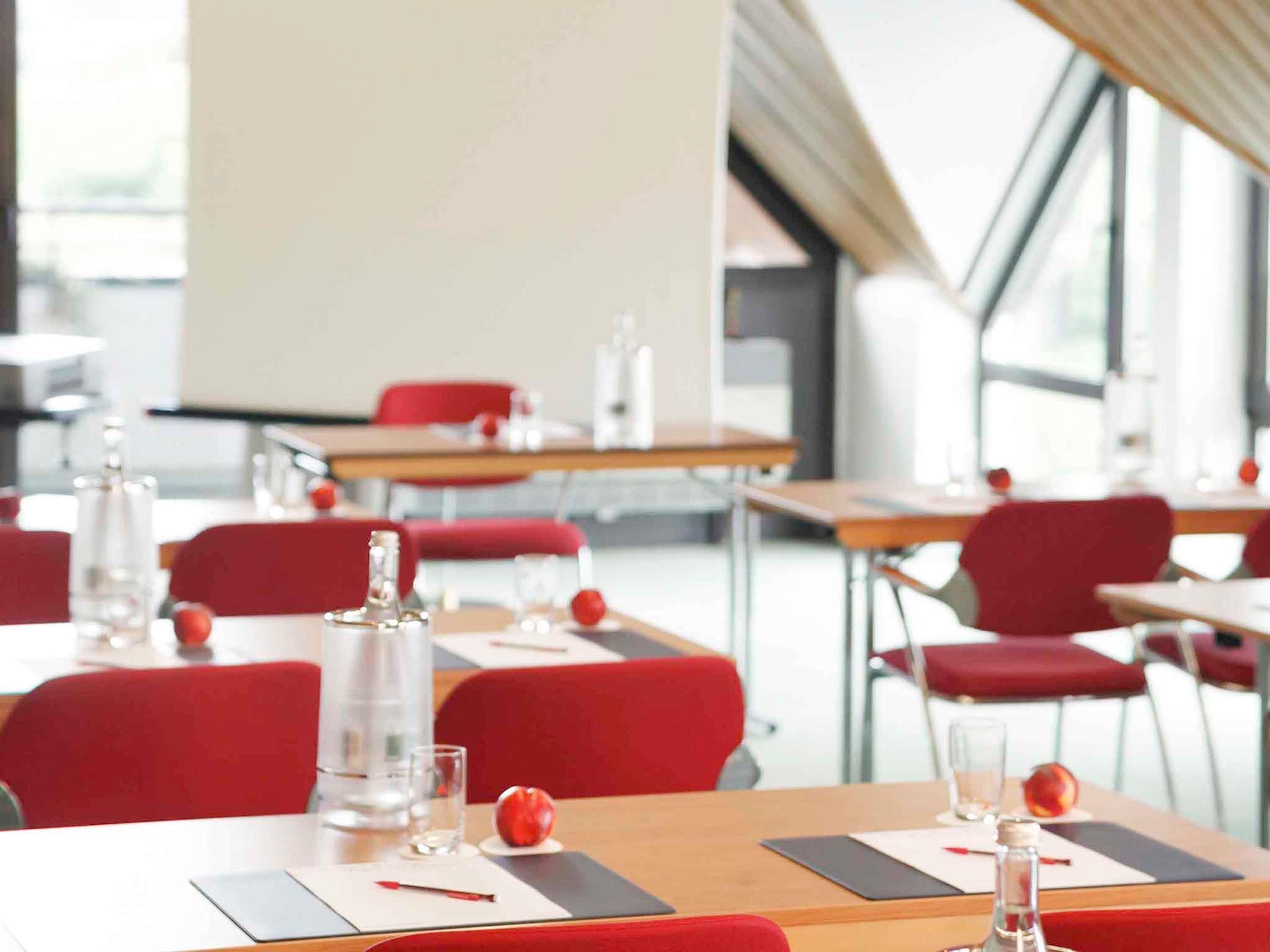 A modern conference room with red chairs, tables, water bottles, and glasses.