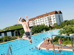 Ein Schwimmbecken mit Menschen im Wasser und einer Person, die vom Sprungturm springt.