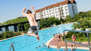 A swimming pool with people in the water and a person jumping off the diving board. - Mercure Bad Duerkheim an den Salinen (Bad Durkheim)