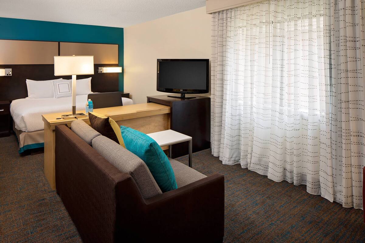 A hotel room with a bed, a sofa, a desk, a television, and a window with curtains.