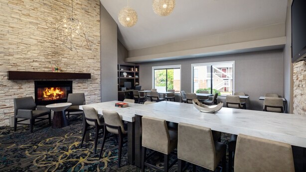 A modern lounge area with a stone wall, a fireplace, and a long table with chairs. There are bookshelves and a television mounted on the wall. - Residence Inn by Marriott Cherry Hill Philadelphia (Cherry Hill)