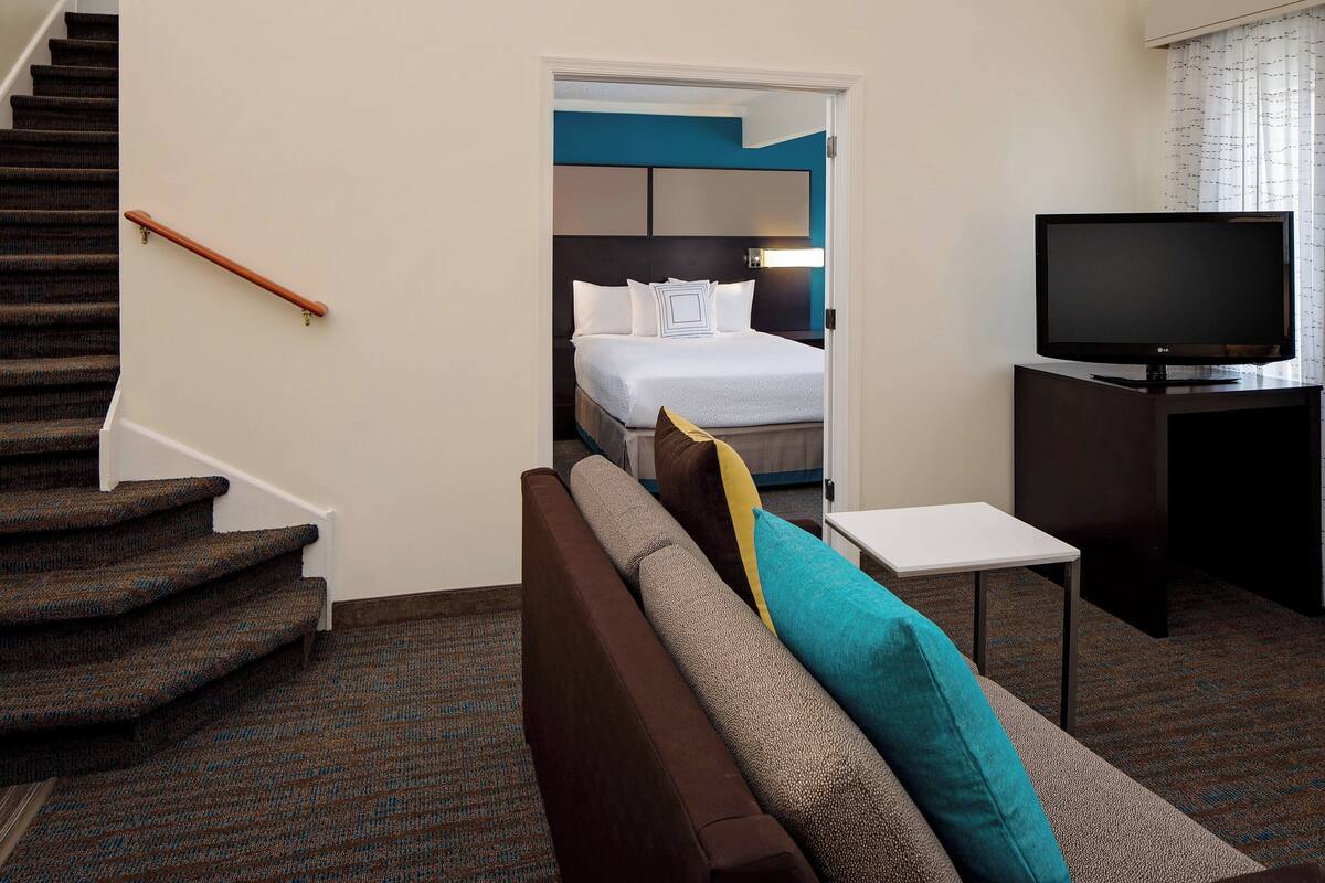 A hotel room with a staircase, a bed with a headboard, a television, and a small table.