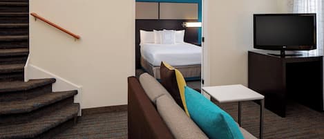 A hotel room with a staircase, a bed with a headboard, a television, and a small table.