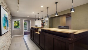 A reception area with a wooden reception desk, pendant lighting, and a view of the outdoors through a window. - Residence Inn by Marriott Cherry Hill Philadelphia (Cherry Hill)
