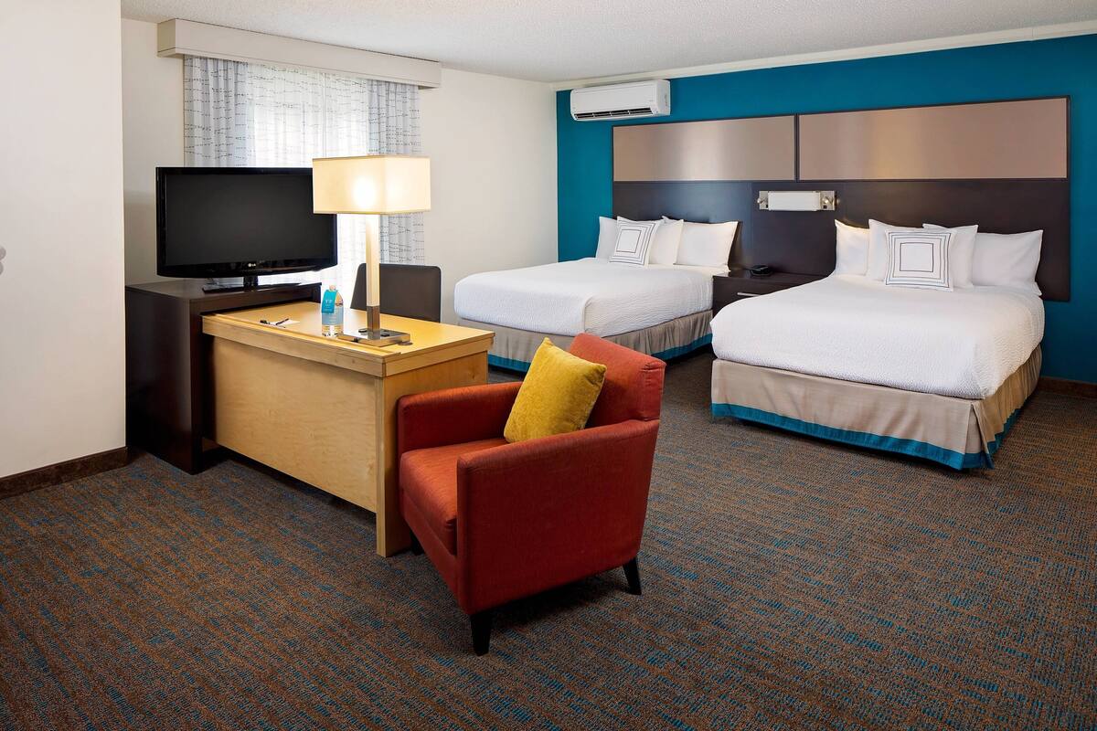 A hotel room with a desk, two beds, a TV, and a chair.