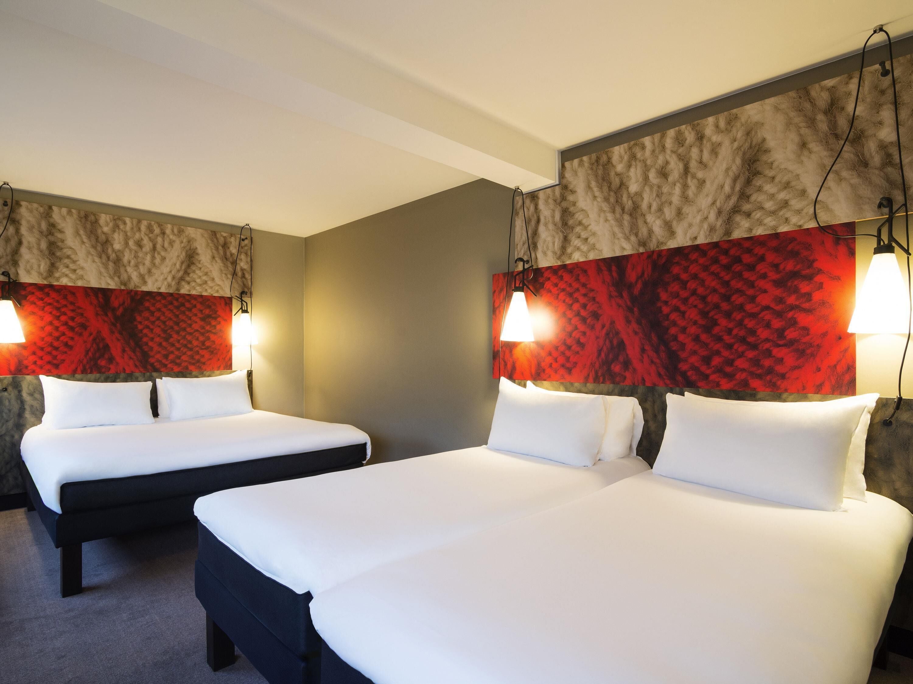 A hotel room with two beds, a grey wall, and a red patterned headboard.