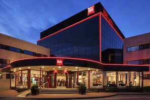 Un hotel moderno con una fachada destacada en rojo y negro, amplias ventanas de vidrio y un área de entrada bien iluminada con asientos exteriores.