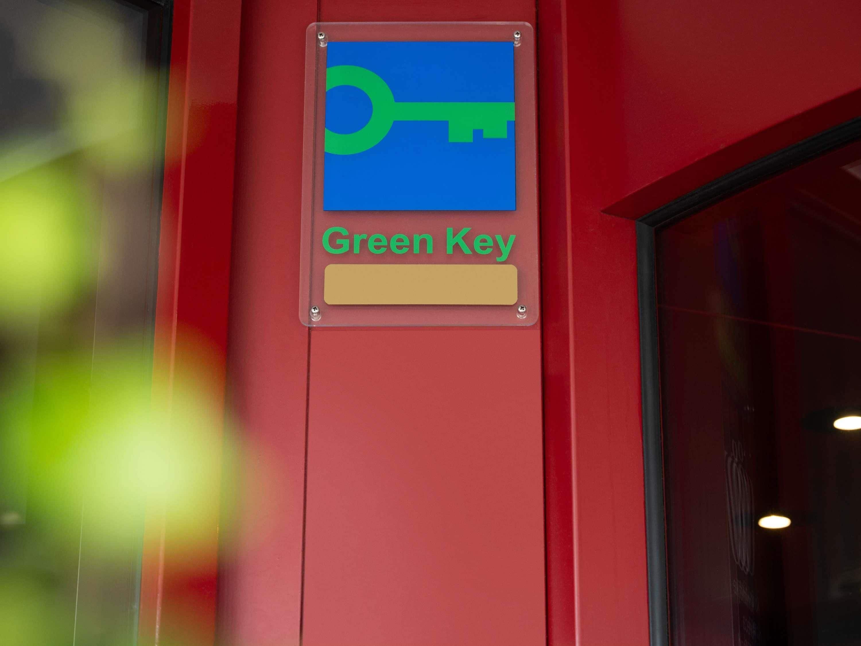 A sign with a key symbol and the text 'Green Key' on a red wall.