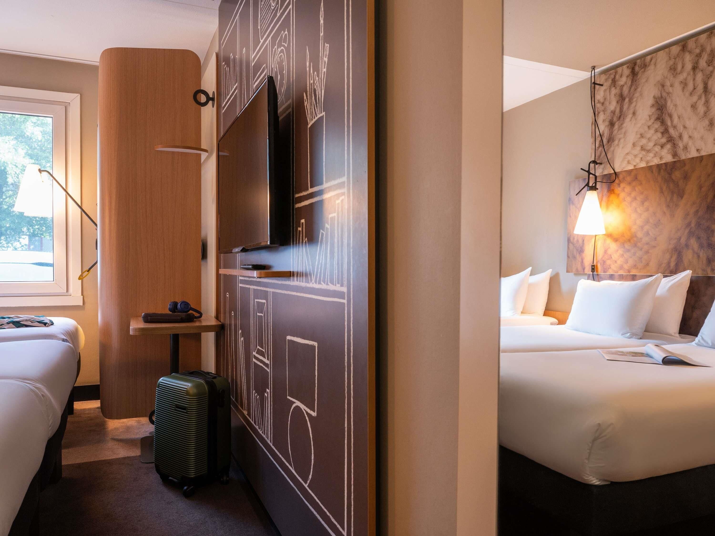 A hotel room with a bed, a desk, a television, and a suitcase.