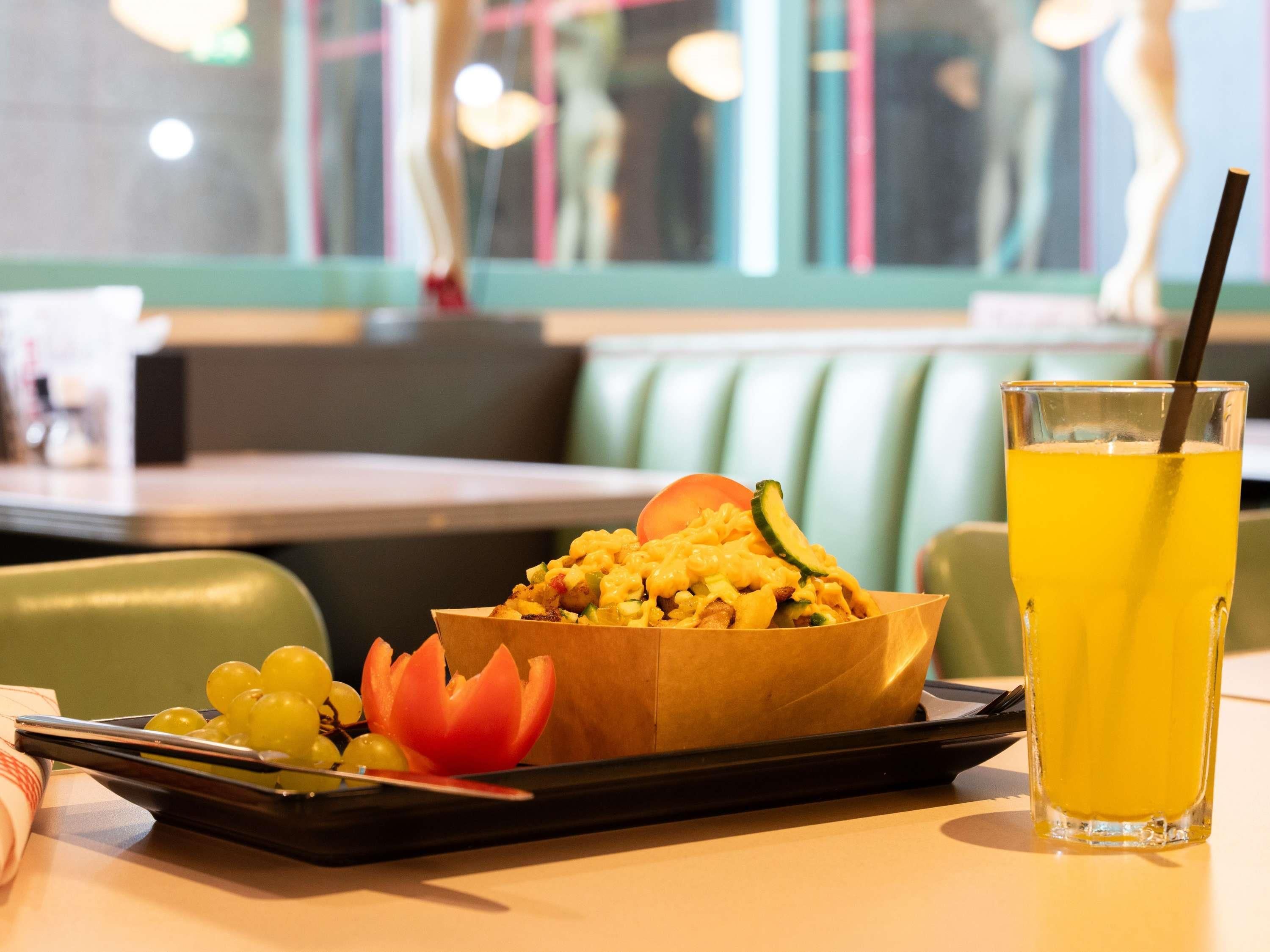 Une scène de restaurant avec une table, un bol de nourriture, un verre de jus d’orange et un plateau contenant des raisins et un fruit décoratif.