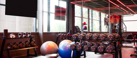 Ein Fitnessraum mit Trainingsgeräten, Bänken und einem großen Spiegel.