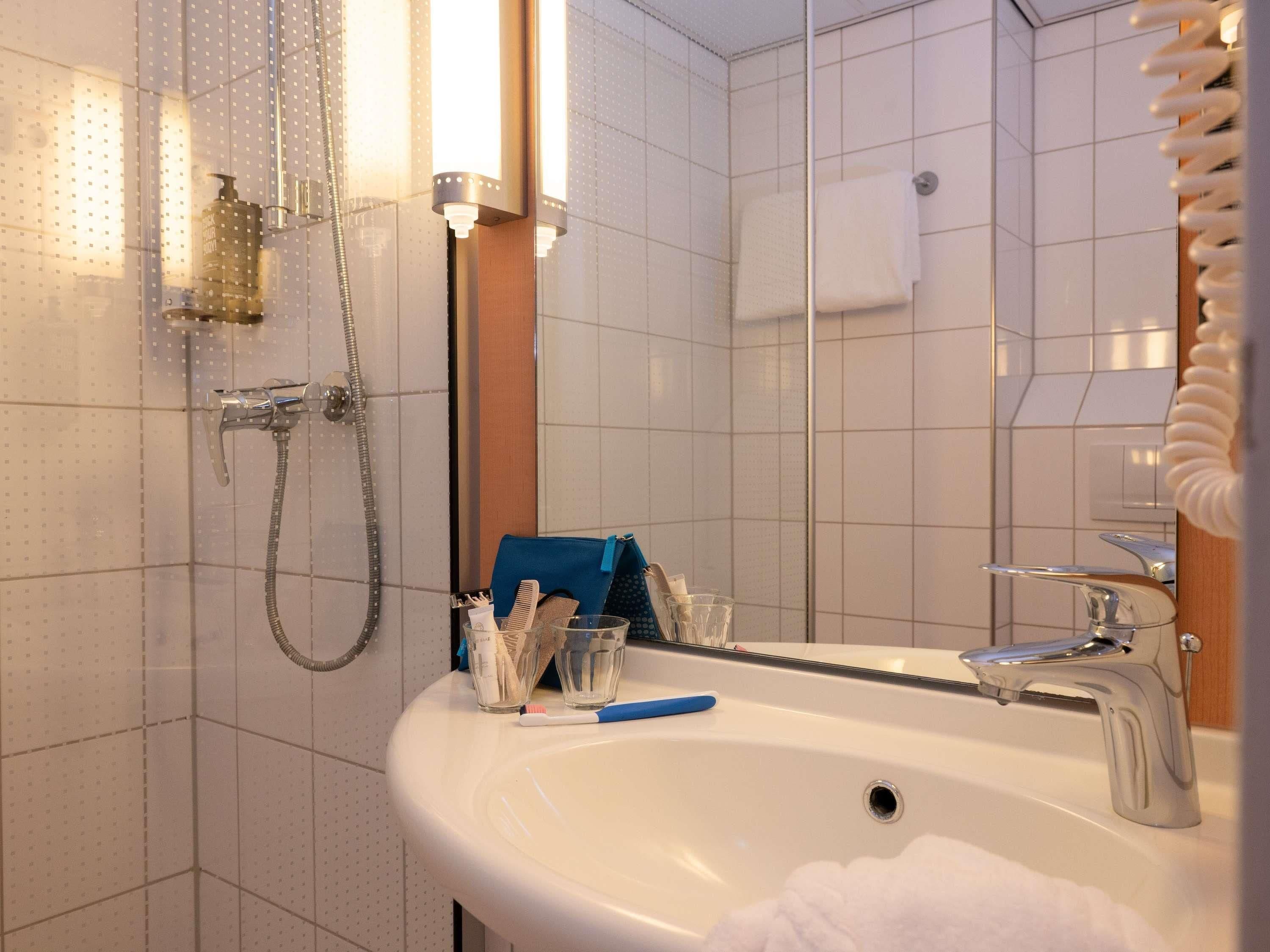 Een badkamer met een witte wastafel, een spiegel, een douche en een handdoekhouder.