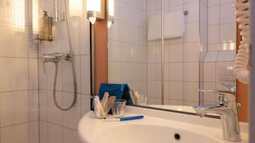 Een badkamer met een witte wastafel, een spiegel, een douche en een handdoekhouder.