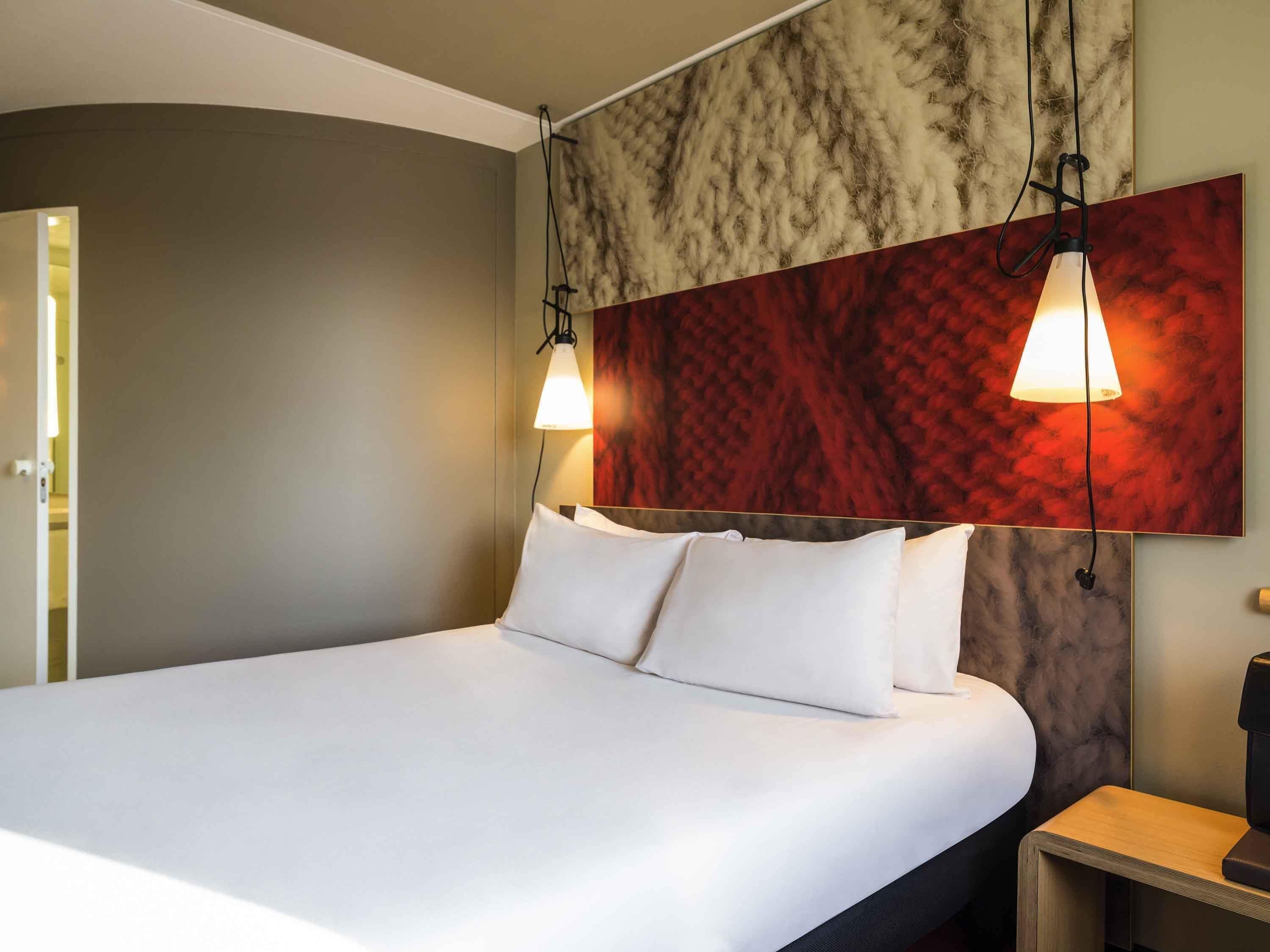 A hotel room with a large bed, two bedside lamps, a wooden nightstand, and a marble-patterned wall.