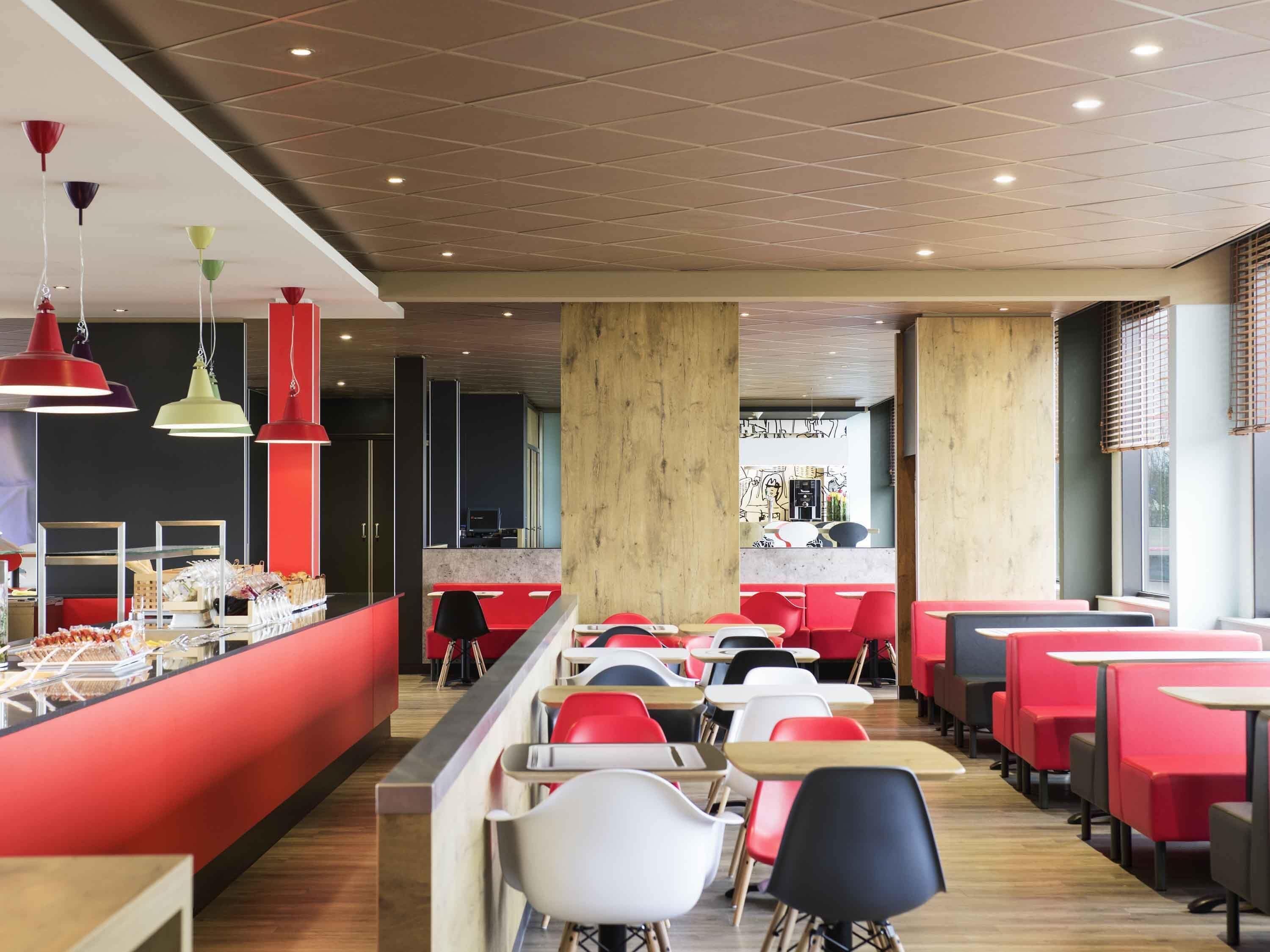 Un restaurante moderno con asientos rojos y blancos, una barra con exhibición de alimentos e iluminación colgante.