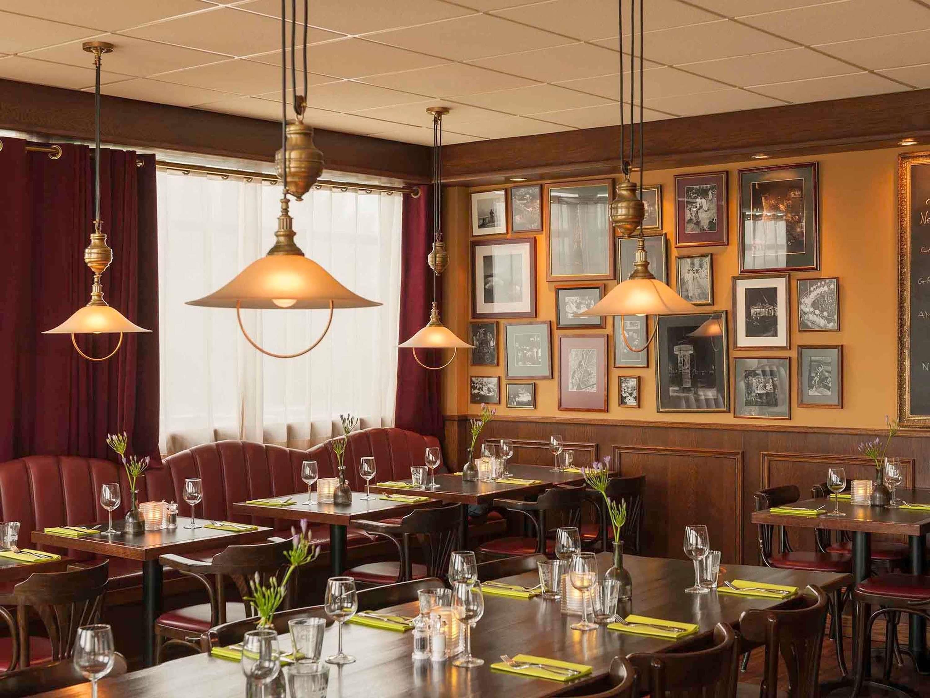 Un interno ristorante con pannelli in legno, quadri appesi alle pareti e tavoli apparecchiati con bicchieri e posate.