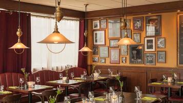 A restaurant interior with wooden paneling, framed pictures on the walls, and tables set with glasses and cutlery.