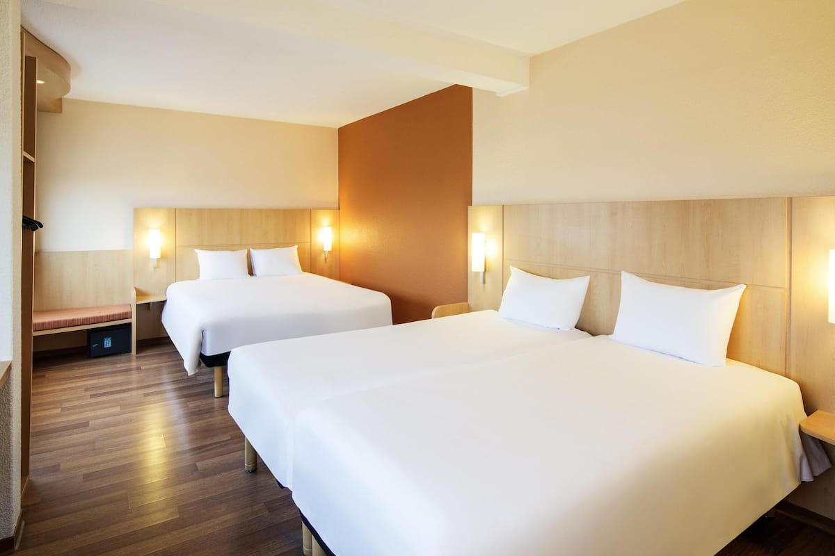 A hotel room with two beds, wooden headboards, bedside tables, and wall-mounted lamps.