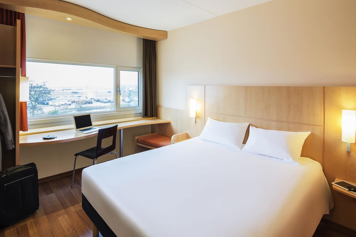 A hotel room with a bed, desk, chair, and a view of the city.