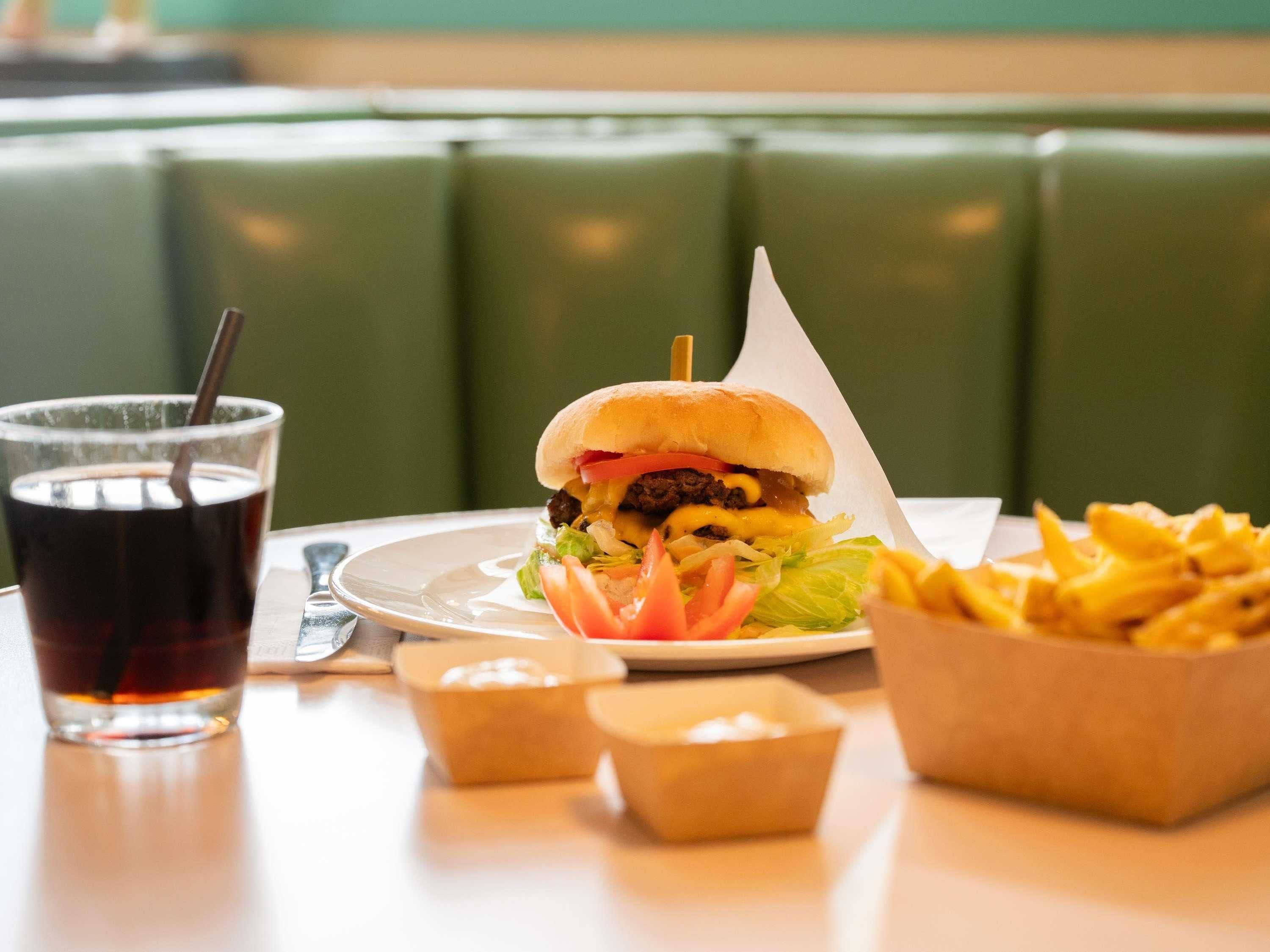 A meal consisting of a burger, fries, and a drink on a table with a green cushioned booth in the background.