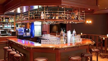 A bar area with a wooden bar counter, multiple stools, and a variety of bottles and glasses.