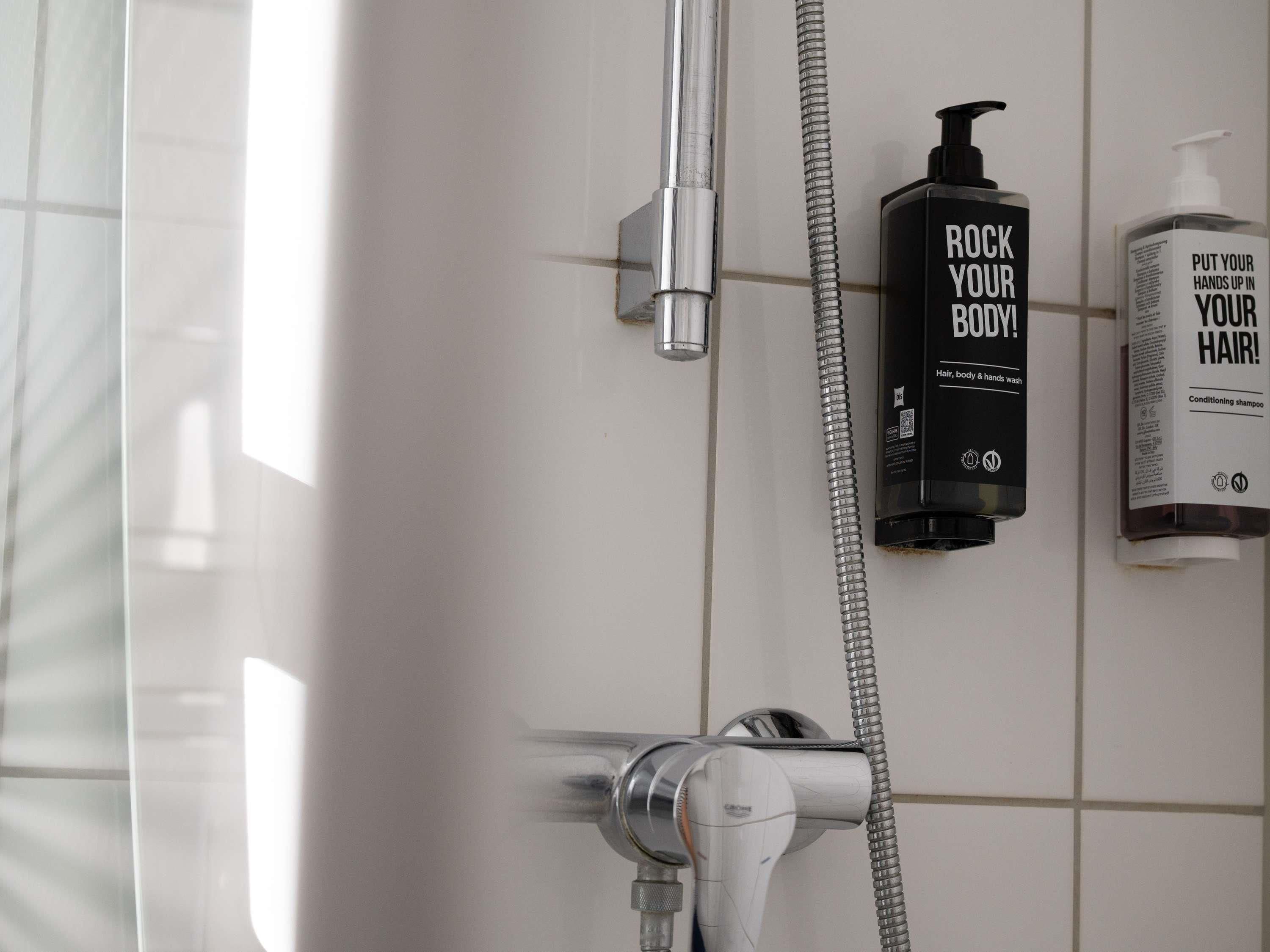 Ein Badezimmer mit Dusche, Duschbrausehandstück und zwei Shampoo-Flaschen.