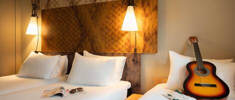 Een hotelkamer met twee bedden, een gitaar en een lampje aan de muur.