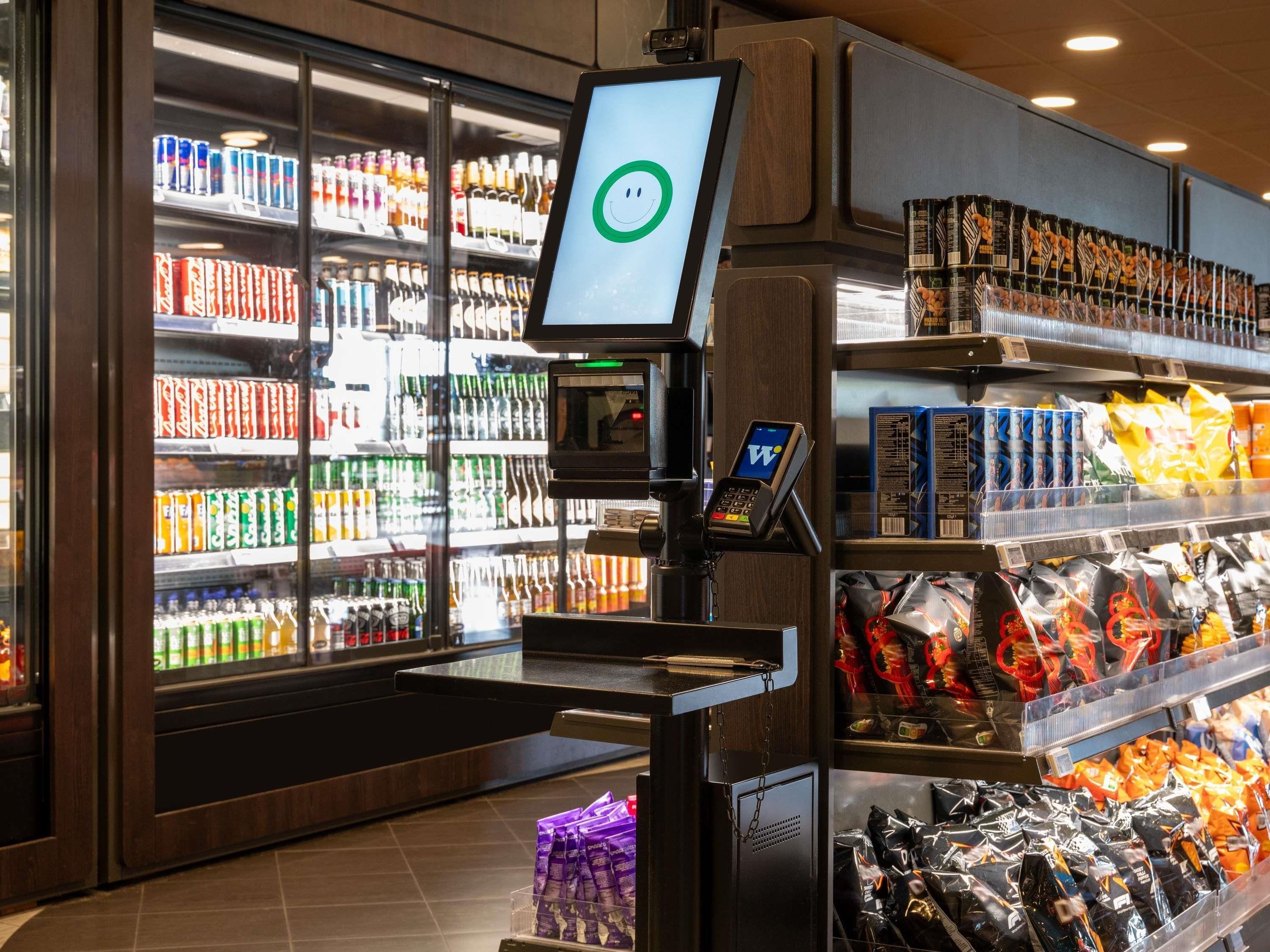 A self-service beverage kiosk with a digital screen, surrounded by shelves stocked with various drinks and snacks.