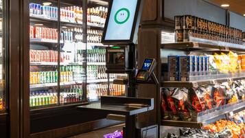 A self-service beverage kiosk with a digital screen, surrounded by shelves stocked with various drinks and snacks.