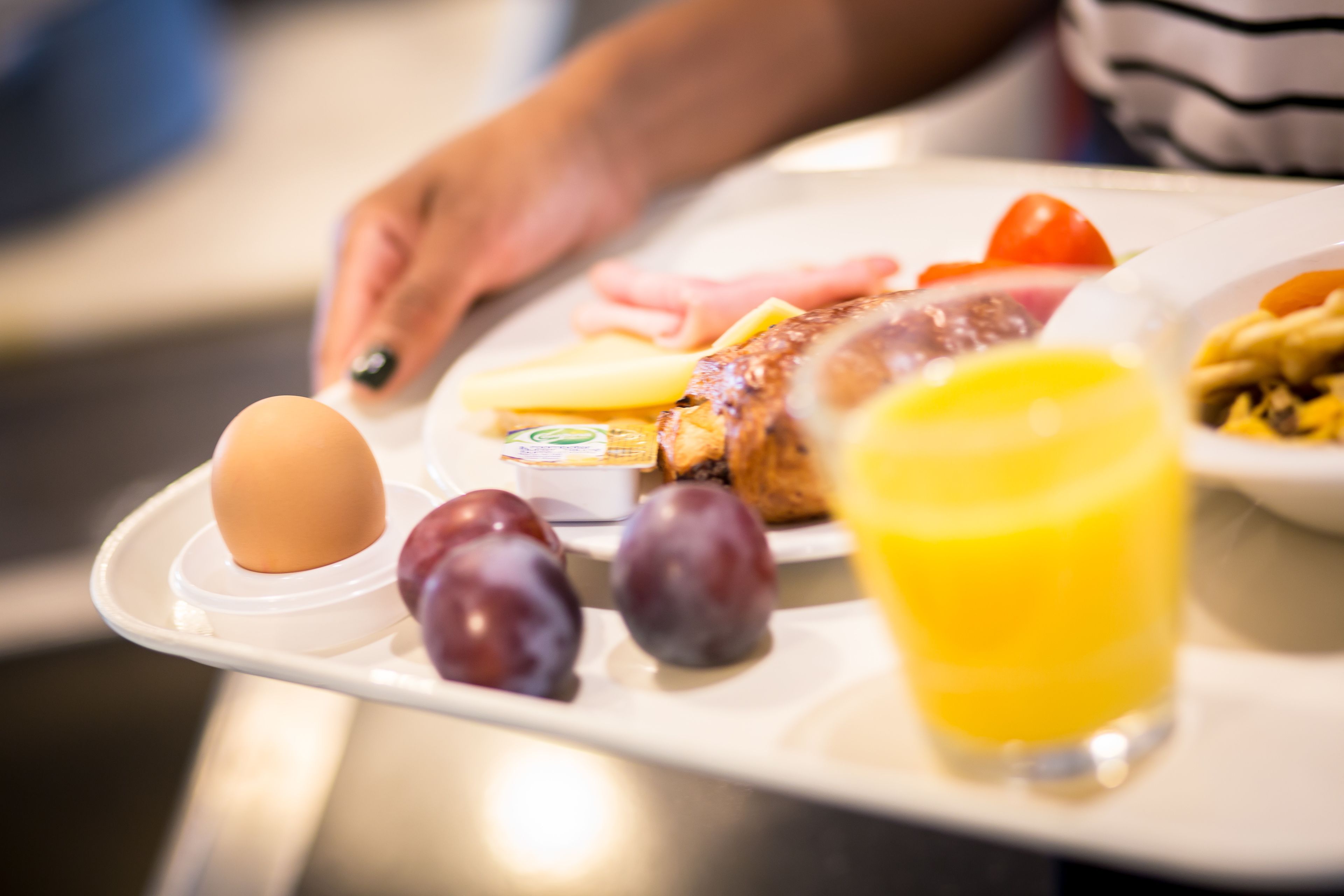 Ein Tablett mit einem gekochten Ei, Pflaumen, einem Glas Orangensaft und einem Teller mit Toast, Tomaten und einem Stück Fleisch.