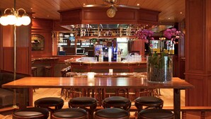 A bar area with a wooden bar counter, stools, and a ceiling fan.