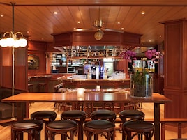 Zona de bar con mostrador de madera, taburetes y un ventilador de techo.