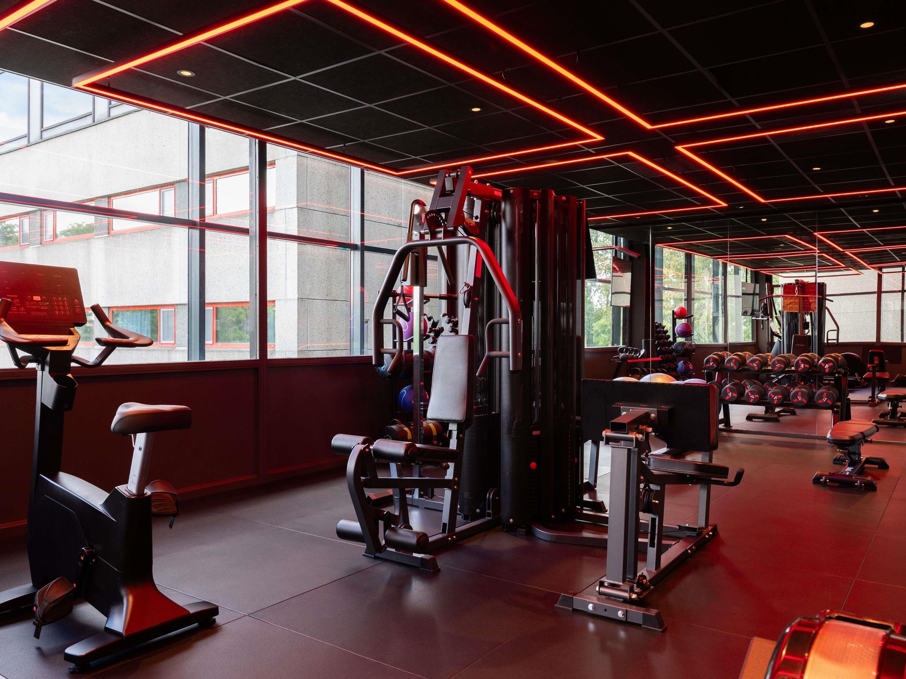 A gym with exercise equipment, large windows, and a red neon ceiling.