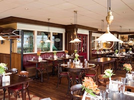 Interior de restaurante con mesas de madera, asientos tapizados en rojo y lámparas colgantes.
