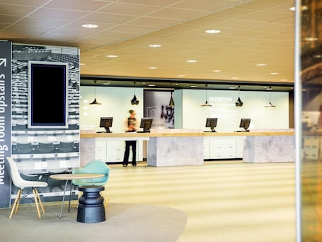 Ein Empfangsbereich mit modernem Design, eine Sitzecke mit Tisch und Stühlen sowie ein großes digitales Display.. Hotel ibis Schiphol Amsterdam Airport