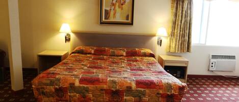 A hotel room with a large bed, two bedside lamps, a framed picture on the wall, a window with curtains, and an air conditioning unit.