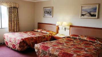 A hotel room with two beds, a headboard, a nightstand with lamps, and two wall-mounted paintings.