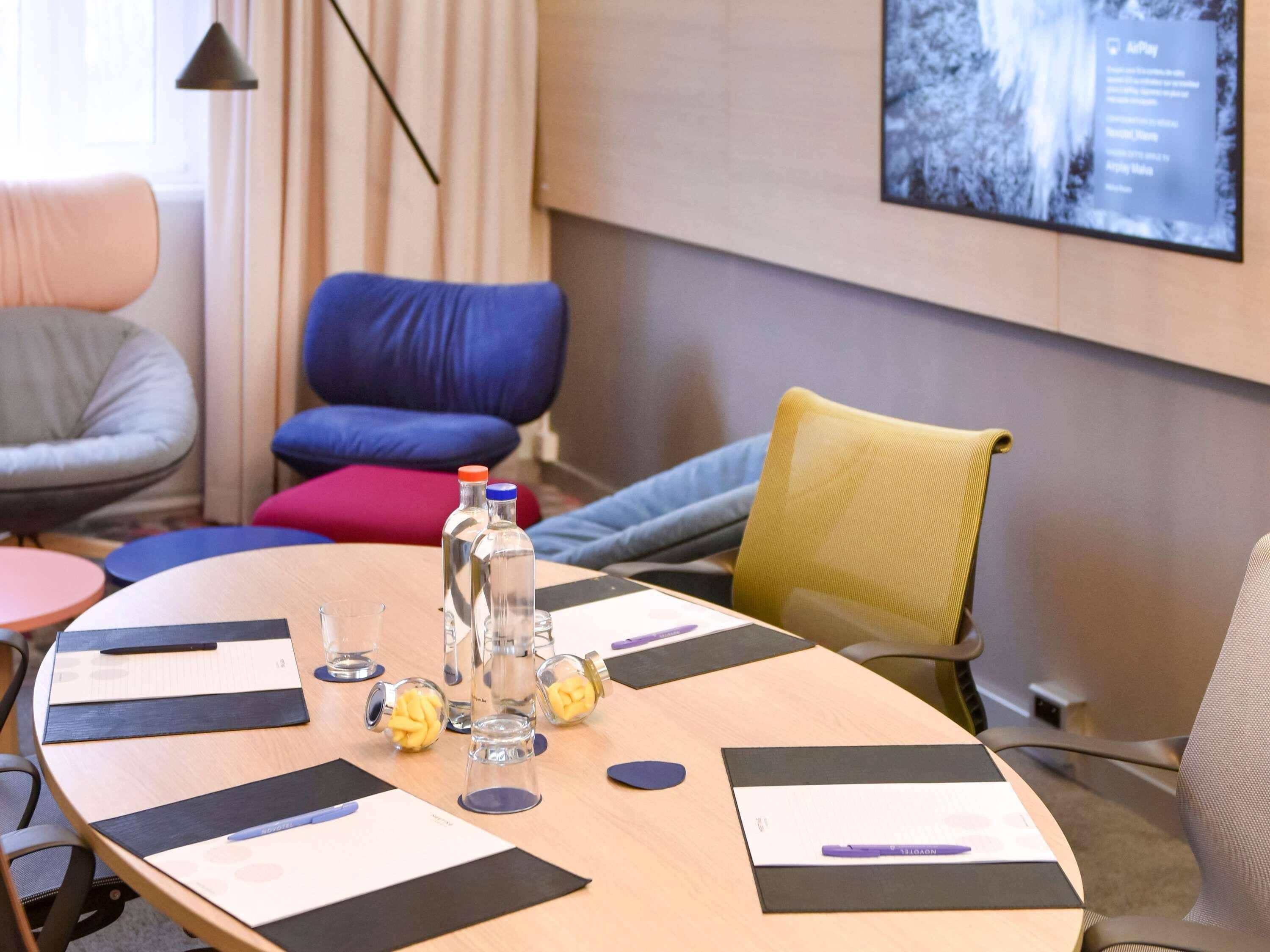 A conference room with a round table, chairs, a projector screen, and a window with curtains.