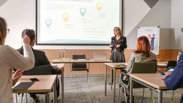 A presentation in a conference room with a screen displaying 'Benefits of Hiring a Presentation Firm.'