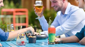 Un grupo de personas sentadas en una mesa al aire libre, con bebidas y aperitivos.