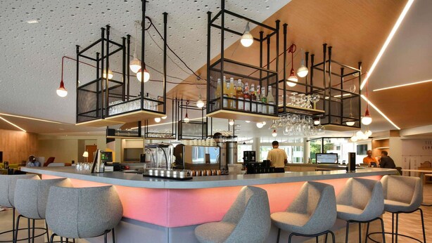 Zona de bar moderna con una barra central, taburetes y luces colgantes.