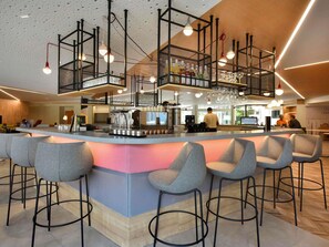 Zona de bar moderna con una barra central, taburetes y luces colgantes.