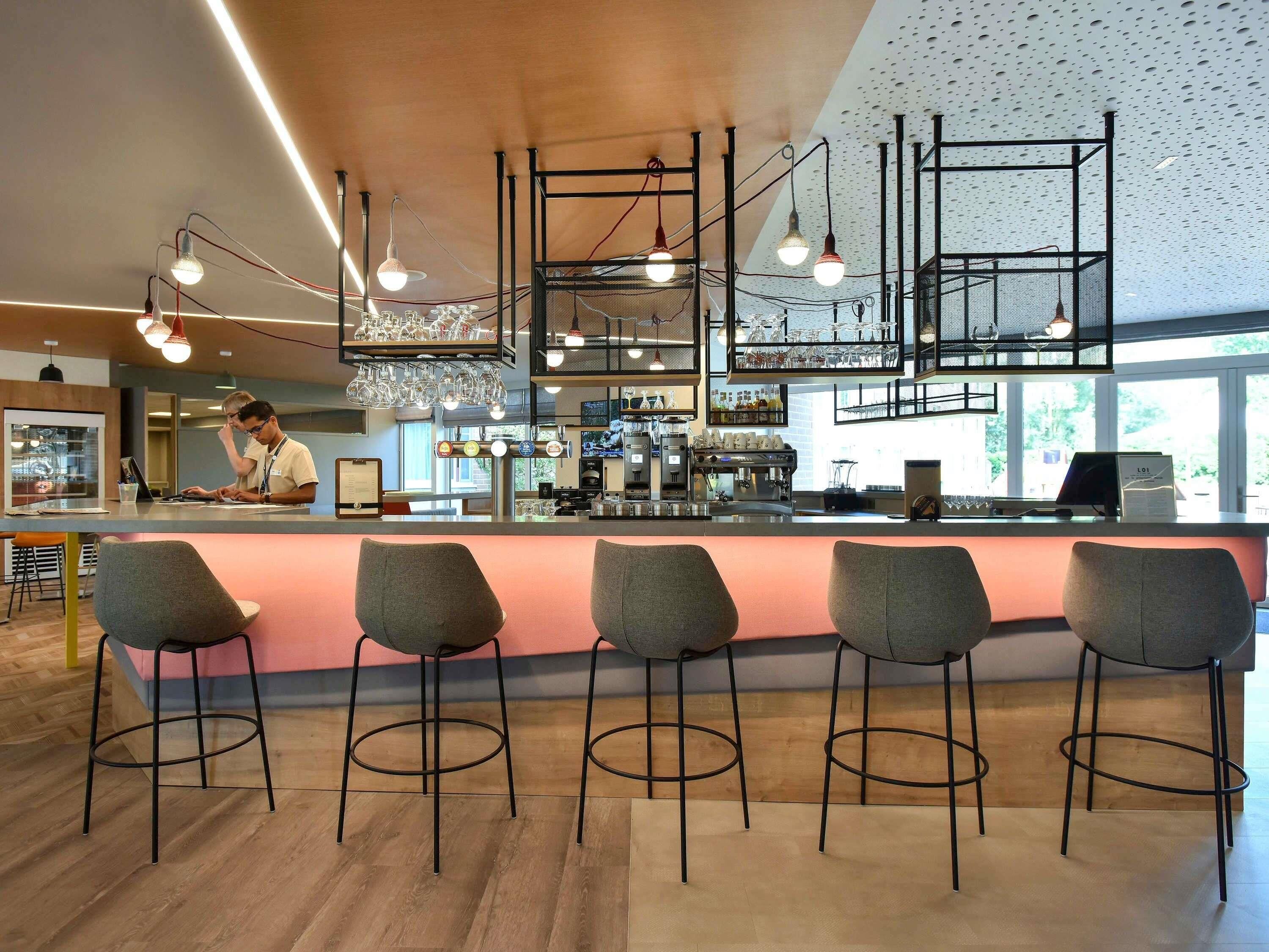 A modern bar area with bar stools, a counter, and overhead lighting fixtures.