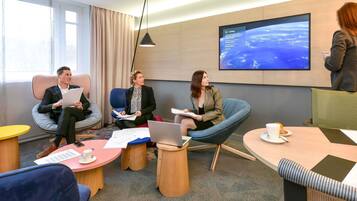 A modern conference room with comfortable seating, a large screen displaying a satellite view, and a casual meeting setup.