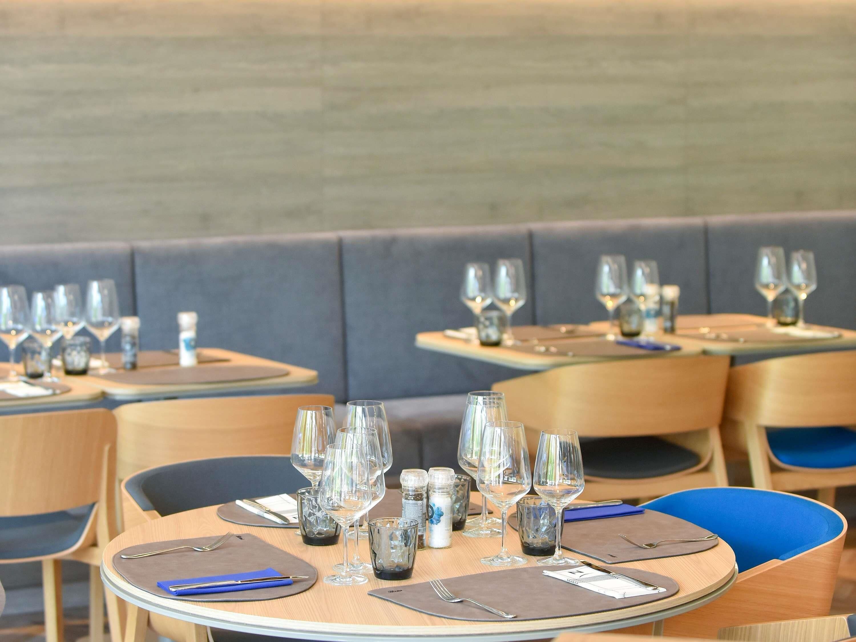 A restaurant with round tables, each set with wine glasses, cutlery, and menus.