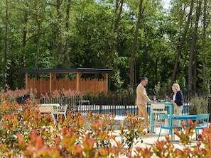 An outdoor seating area with tables and chairs, surrounded by greenery and trees. - Novotel Wavre Brussels East Hotel (Wavre)