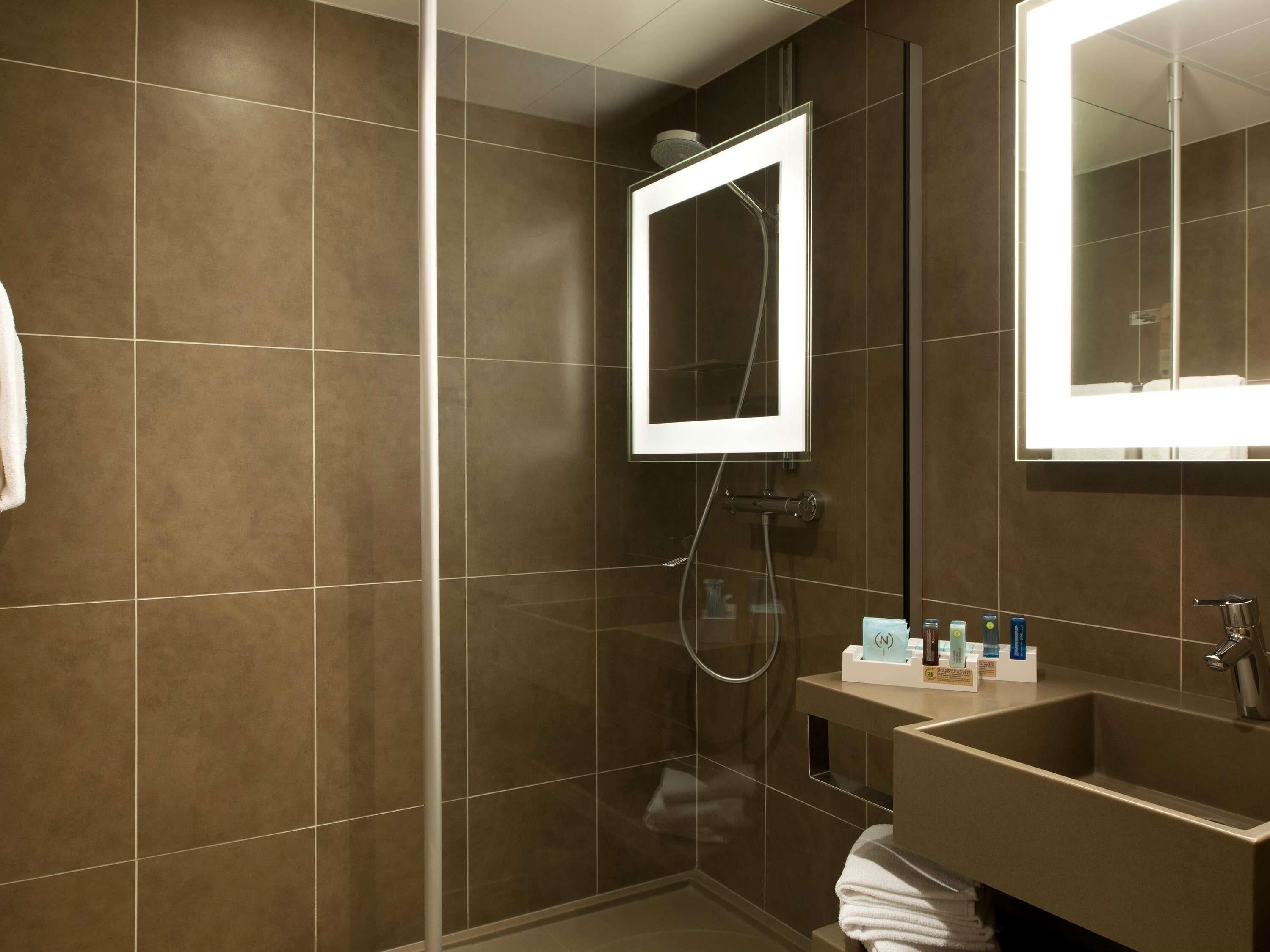 A modern bathroom with a glass-enclosed shower, a vanity with a sink, and a mirror with integrated lighting.