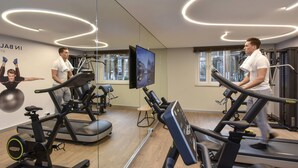 Un gimnasio con cintas de correr, bicicletas estáticas y una pantalla de televisión.